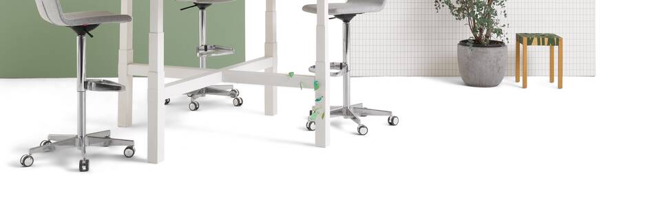 Gispen TMNL Agile 4 leg table in white with light beech tabletop in standing position with grey Triennial Work high chairs with backpanels front right view