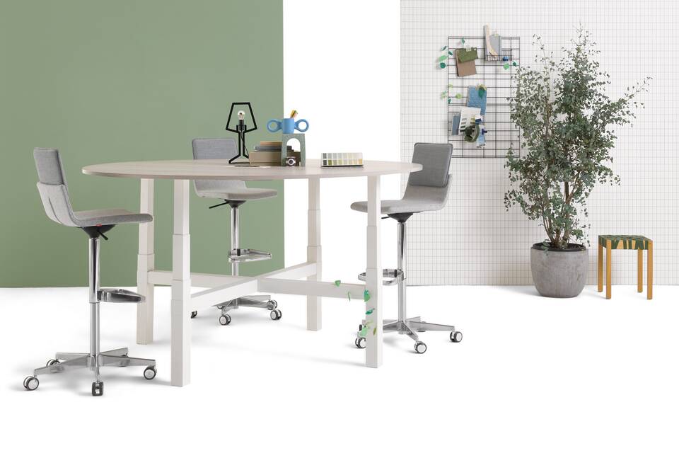 Gispen TMNL Agile 4 leg table in white with light beech tabletop in standing position with grey Triennial Work high chairs with backpanels front right view