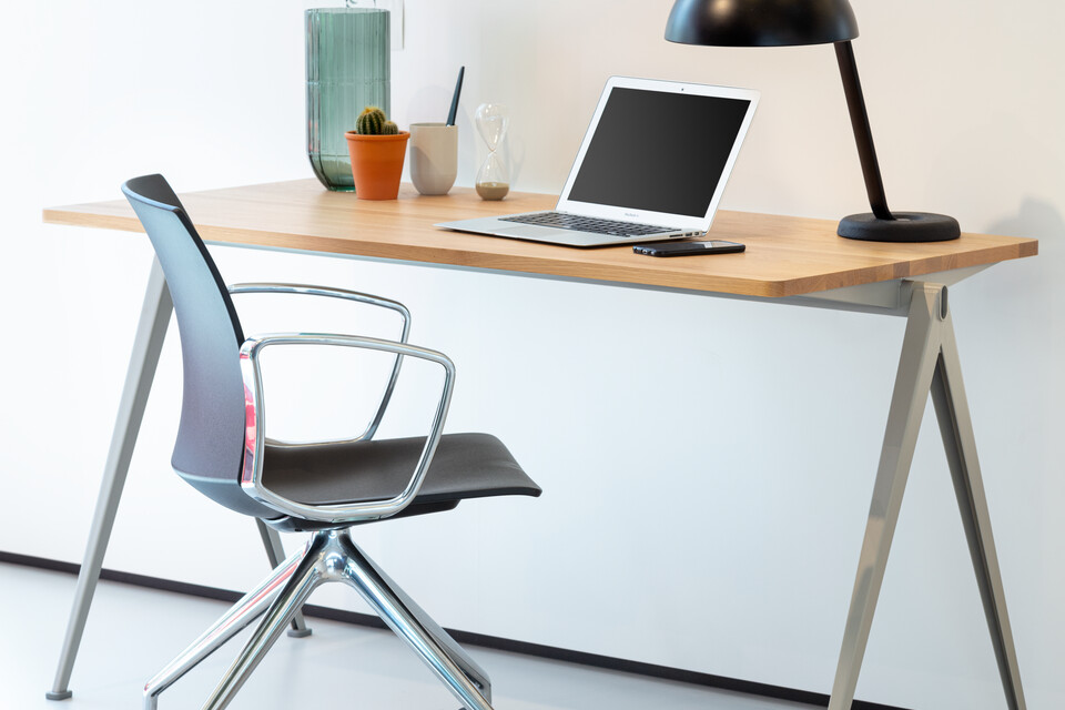 Royal Ahrend Well trestle base chair on castors with polished chrome frame and armrests with anthracite shell turned open and Pyramid table left rear view