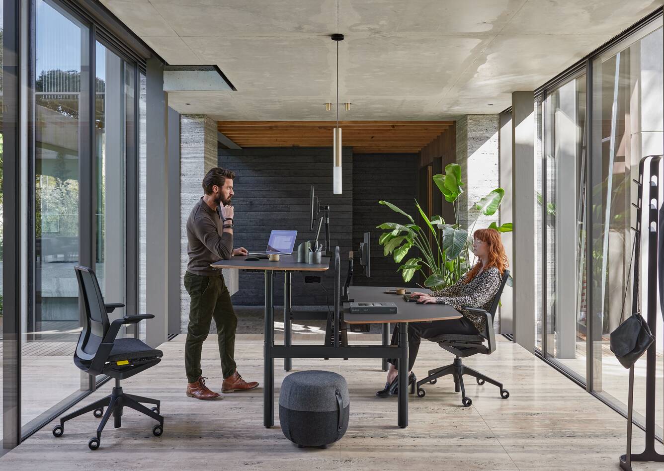 Ahrend Remode office chairs in black with Modea dual workstation and Recharge pouf with 2 models and 1 standing in a work setting side view