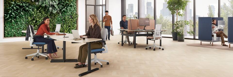 Ahrend Modea sit stand solo workstations in white and oak wave tabletops with sitting models in a vitalising workspace interior view