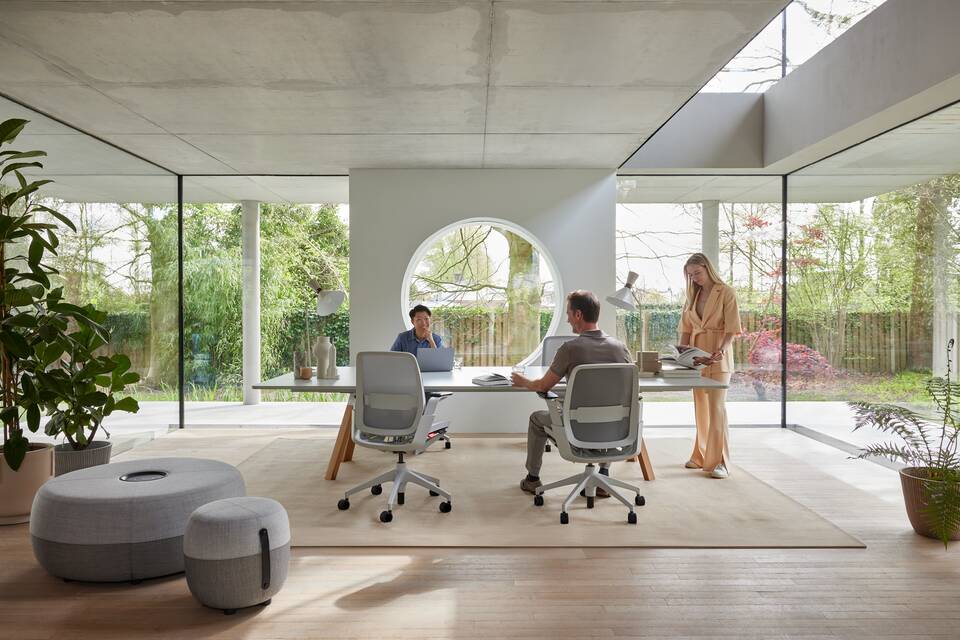 Ahrend Remode office chairs in grey with lumbar support and an Aero bench with Recharge poufs with 3 models in a colaborative setting interior view