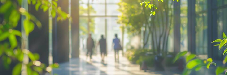 Blurred background of people walking in a modern office building with green trees and sunlight , eco friendly and ecological responsible business concept image with copy space