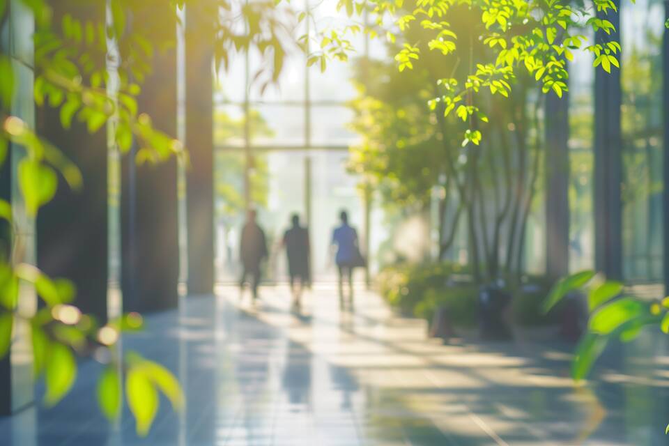 Blurred background of people walking in a modern office building with green trees and sunlight , eco friendly and ecological responsible business concept image with copy space