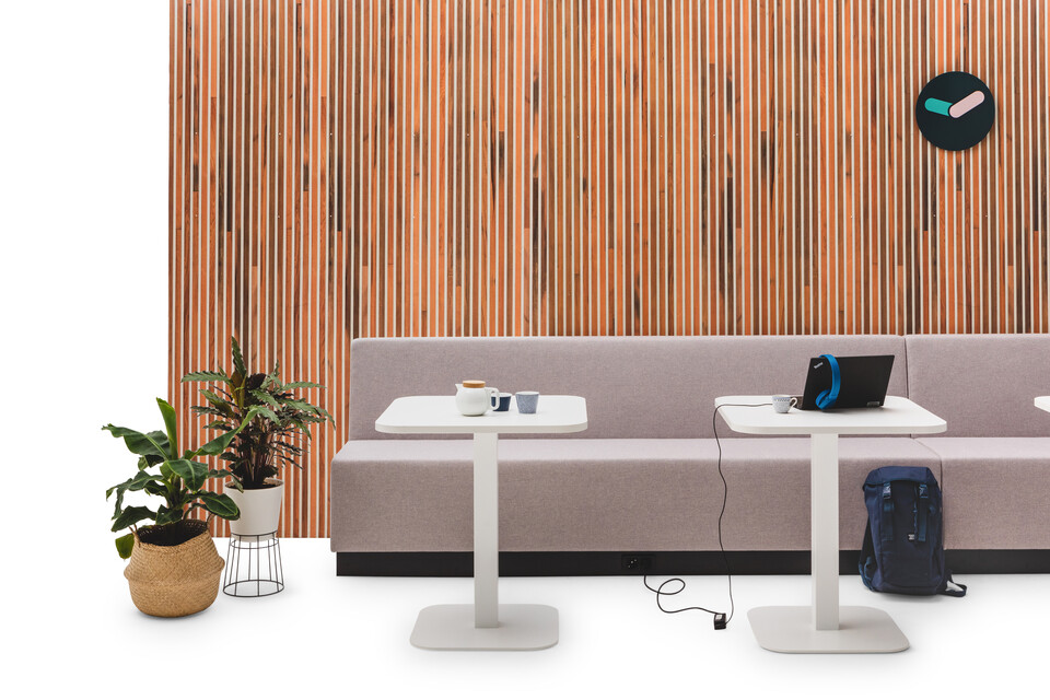 Gispen JUNA Single low trainbench upholstered in grey with 2 white KOLM column tables in front of brown wood patern backpanel front view