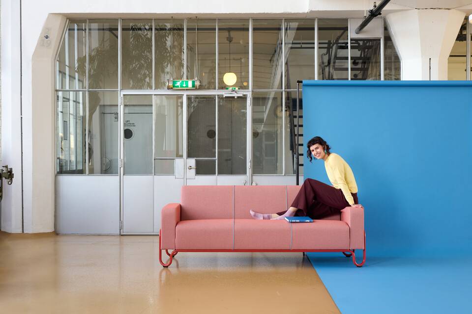 Gispen Classics 441 sofa in red with orange red upholstered seat and back partially on blue backdrop with female model coffee roastery at Van Nelle factory front view