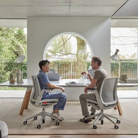 Ahrend Remode office chairs in grey and an Aero bench with Recharge poufs with 2 models in a colaborative setting interior view