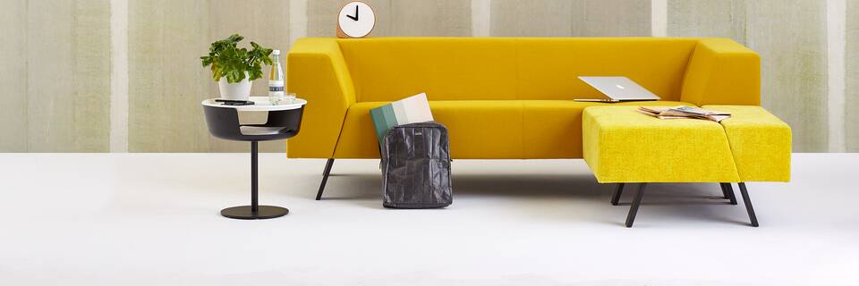 Gispen Sett sofa with yellow upholstery and Asy sidetable with Slingerlamp pendant lamp with plant and laptop in front of light green background front view