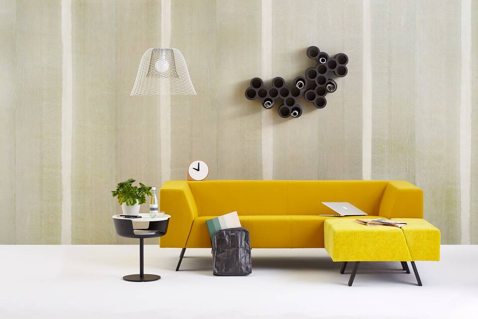 Gispen Sett sofa with yellow upholstery and Asy sidetable with Slingerlamp pendant lamp with plant and laptop in front of light green background front view
