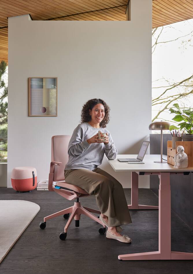 Ahrend Remode office chair in pink with balance solo workstation and model holding cup in a home setting right side view