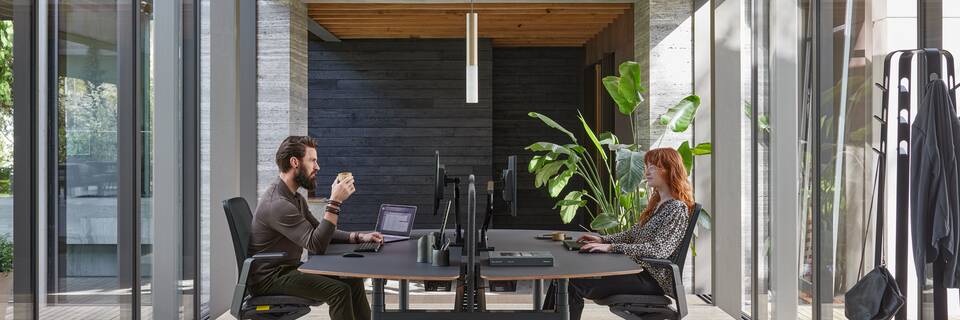 Ahrend Remode office chairs in black with Modea dual workstation and Recharge pouf with 2 models in a work setting side view