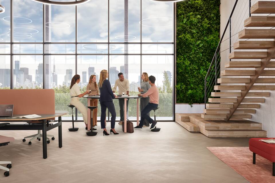 Ahrend Modea sit stand conference table in pink with grey round tabletop in stand height with sitting and standing models in a vitalising workspace interior view