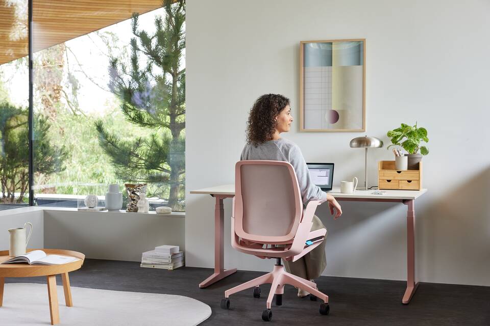 Ahrend Remode office chair in pink with balance solo workstation and model looking outside in a home setting rear view
