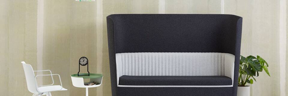 Gispen TST sofa with black and grey upholstery and white Ray pendant lamp with leaves and Asy sidetable and Outline clock with Nomi Wood in front of light green background front view