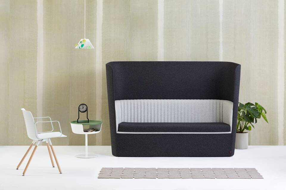 Gispen TST sofa with black and grey upholstery and white Ray pendant lamp with leaves and Asy sidetable and Outline clock with Nomi Wood in front of light green background front view