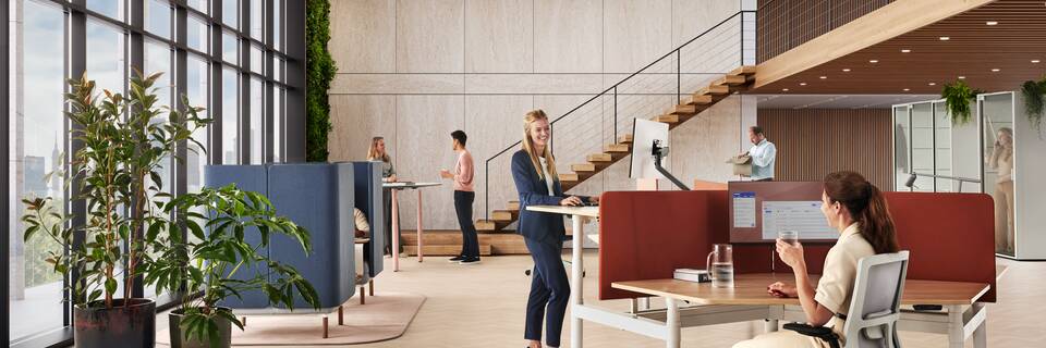Ahrend Modea sit stand trio workstation in white with oak tabletop and orange S25 screens with models in a vitalising workspace interior view