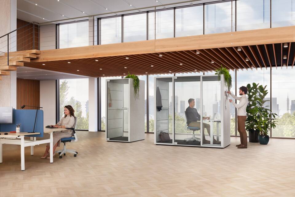 Ahrend Qabin Call and Chat Focus space in space in grey and white Modea trio workstation with blue S25 screen with sitting and standing models in a vitalising workspace interior view