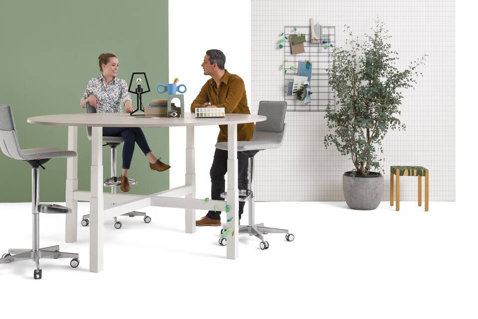 Gispen TMNL Agile 4 leg table in white with light beech tabletop in standing position with grey Triennial Work high chairs with backpanels and models front right view
