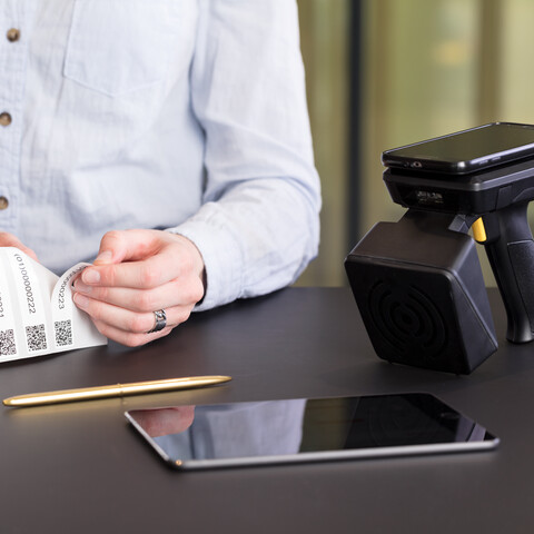 Royal Ahrend service Asset Management with male model peeling off labels with QR code and ipad with scanner with phone front detail view