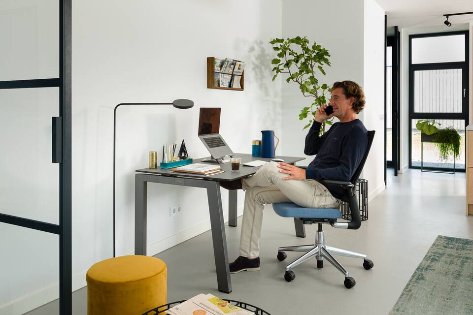 Royal Ahrend balance workstation in grey with charcoal tabletop and 2020 Extra Verta office chair upholstered in blue with male model calling interior view