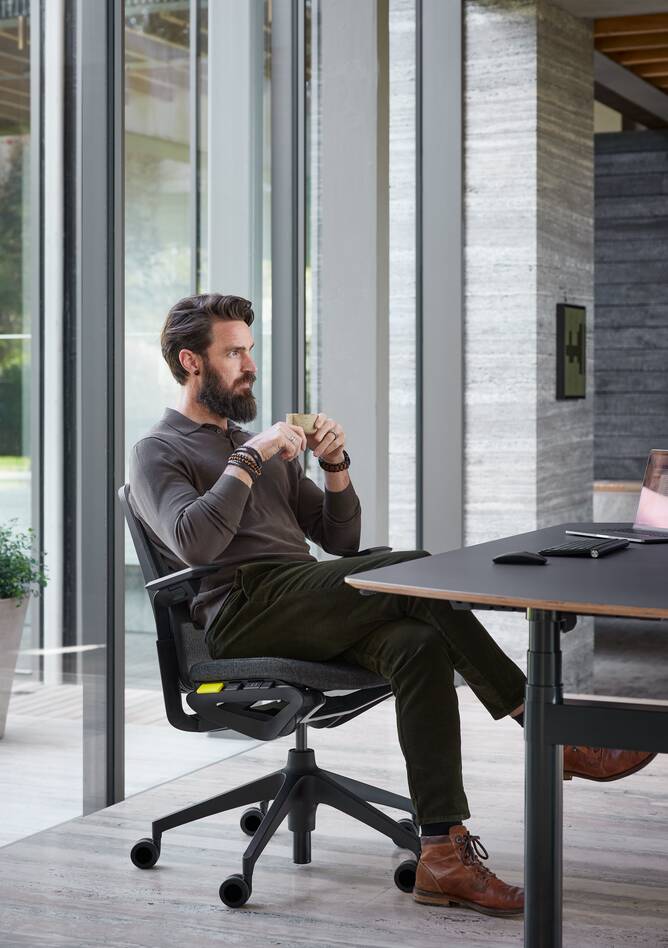 Ahrend Remode office chair with medium high back in black with Modea dual workstation with model drinking in a work setting front left view