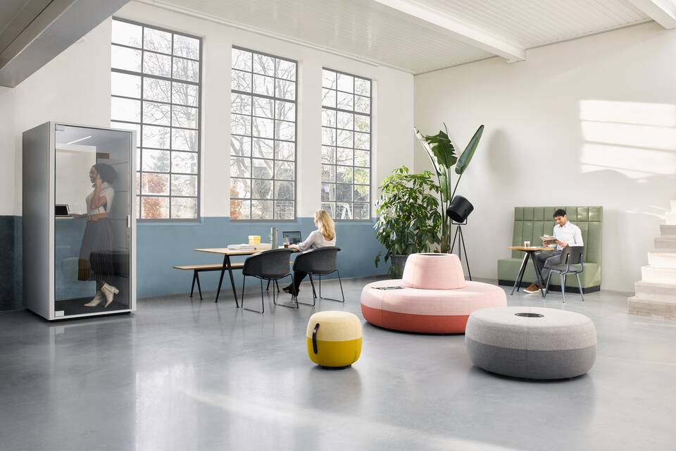 Ahrend Recharge poufs upholstered in pink yellow and grey with Qabin and Pyramid with Well armchairs and models in a Hybrid working community setting