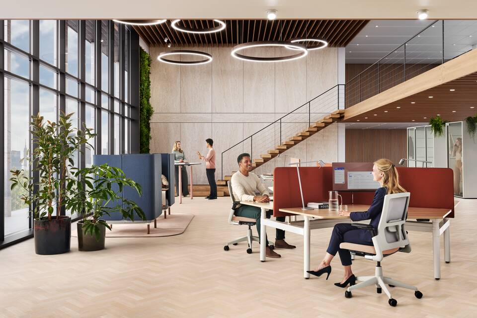 Ahrend Modea sit stand trio workstation in white with oak tabletop and orange S25 screens with sitting models in a vitalising workspace interior view