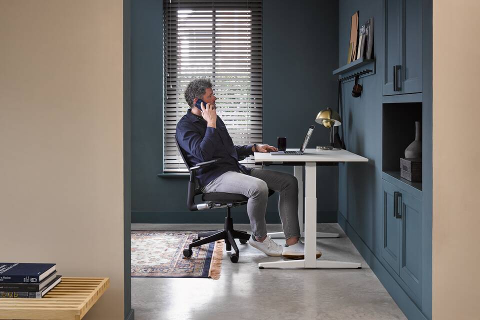 Ahrend Balance workstation in white with black 2020 Verta office chair in a work from home setting with male model calling interior view