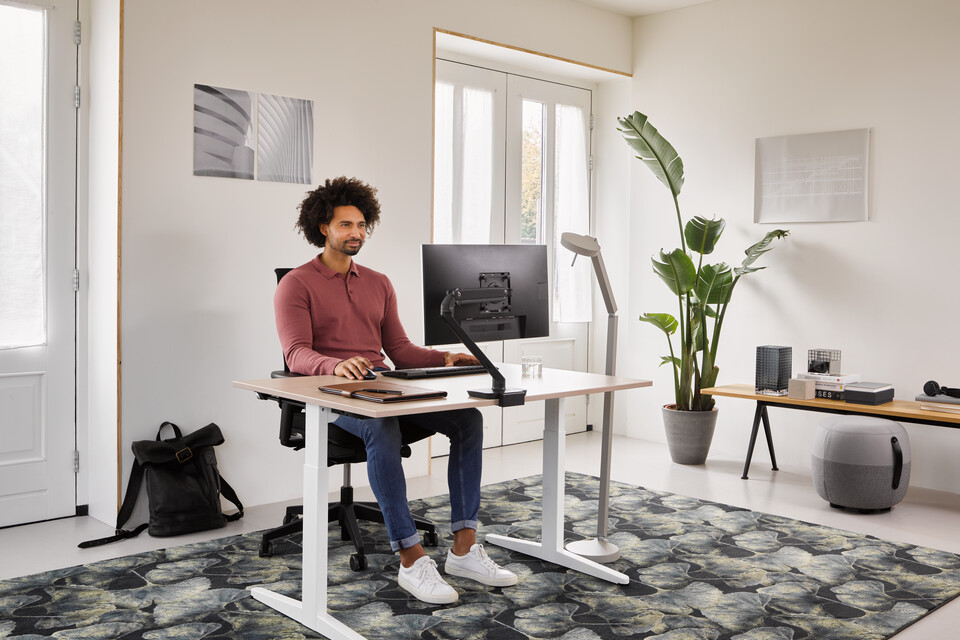 Ahrend Home HVM desk in white with oak tabletop and black Ease office chair with grey Recharge and Pyramid bench with male model thinking in a work from home setting