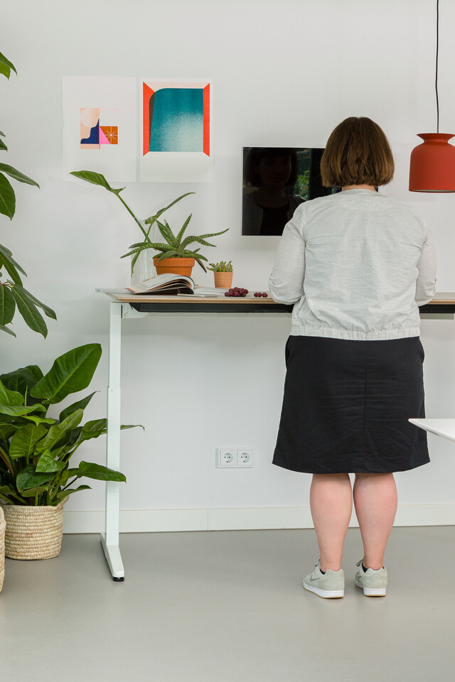 Royal Ahrend balance workstation in white with oak tabletop in standing position with female model interior view