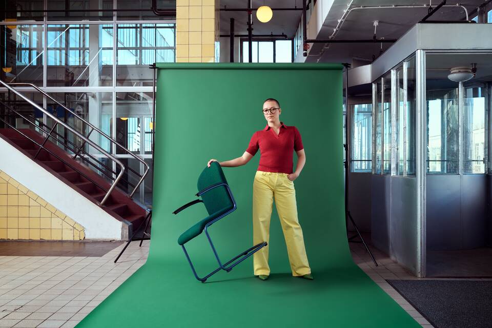 Gispen Classics 413R chair in blue with green upholstered seat and back on green backdrop with female model stairway at Van Nelle factory front right view