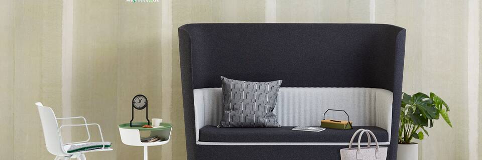 Gispen TST sofa with black and grey upholstery and white Ray pendant lamp with leaves and Asy sidetable and Outline clock with Nomi Wood and styling in front of light green background front view