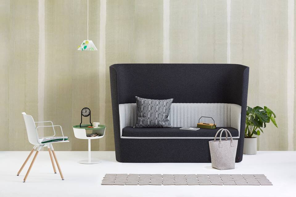 Gispen TST sofa with black and grey upholstery and white Ray pendant lamp with leaves and Asy sidetable and Outline clock with Nomi Wood and styling in front of light green background front view