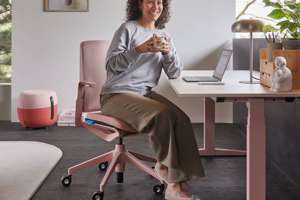 Ahrend Remode office chair in pink with balance solo workstation and model holding cup in a home setting right side view