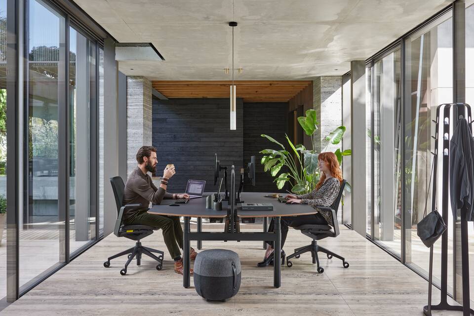 Ahrend Remode office chairs in black with Modea dual workstation and Recharge pouf with 2 models in a work setting side view