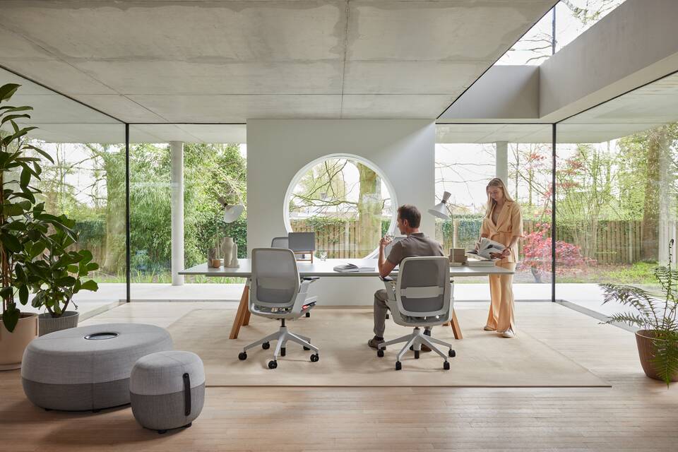 Remode, Aero, Recharge 100, Recharge 45 Ahrend Remode office chairs in grey with lumbar support and an Aero bench with Recharge poufs with 2 models in a colaborative setting rear view